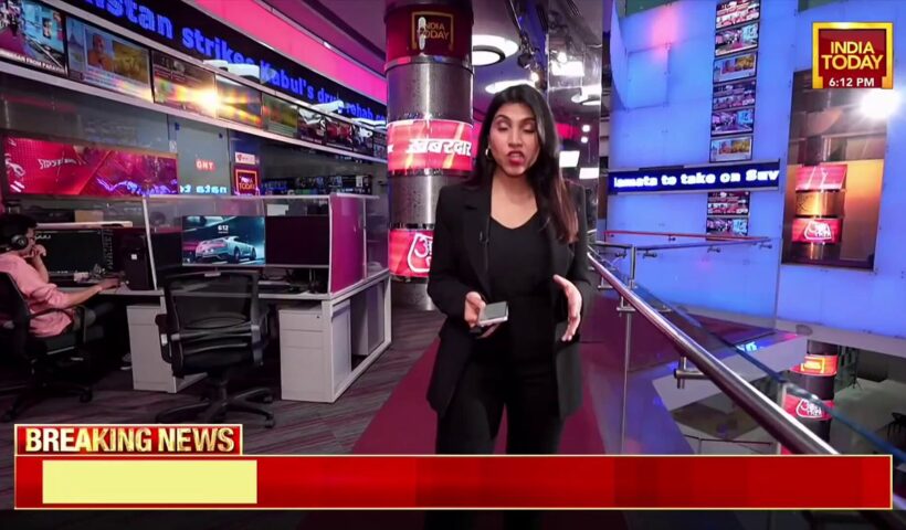 News anchor in a live newsroom with a breaking-news graphic.